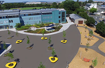 Drohnenansicht auf Pausenhof. Gelbe Sitzinseln jeweils mit Baum in der Mitte